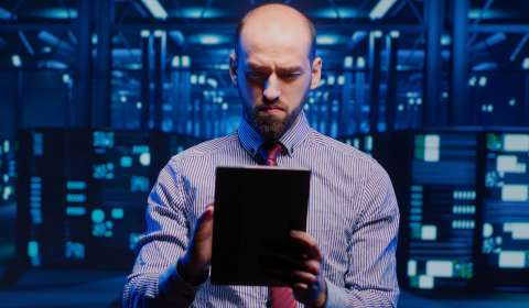 A NOC technician works on a tablet with servers in the background
